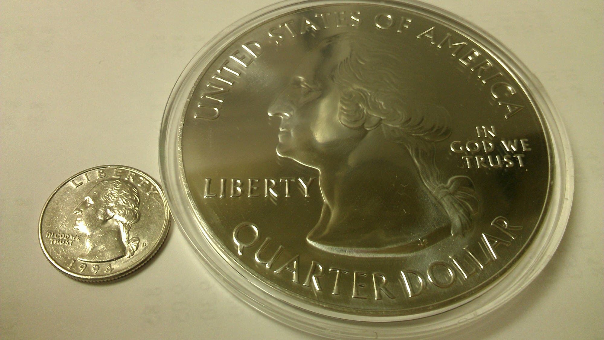 Five-ounce America the Beautiful silver bullion coin beside a quarter.